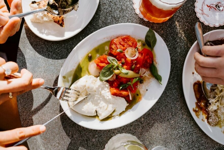 Plates of food on a table, with hands using cutlery to break it apart.