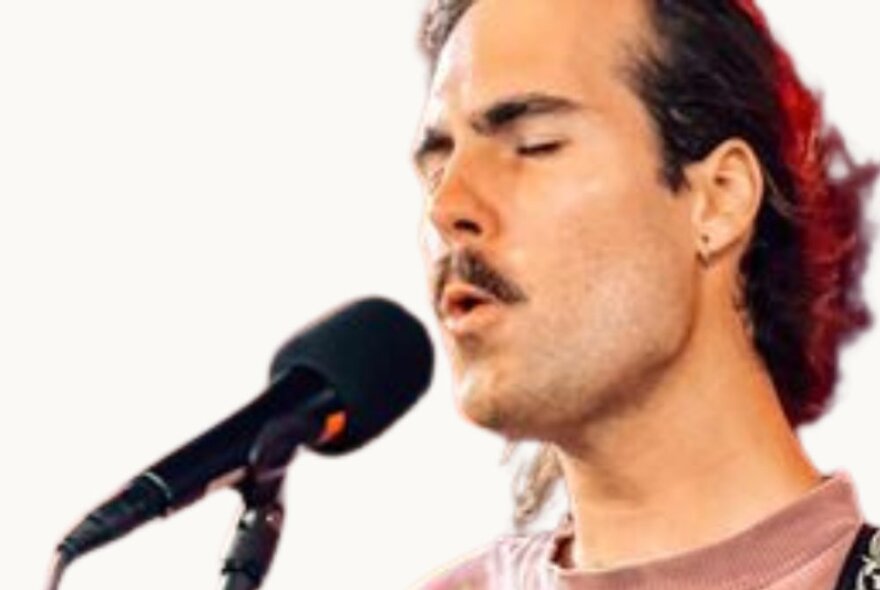 Close-up of a young man's face, singing into a microphone, his eyes closed.