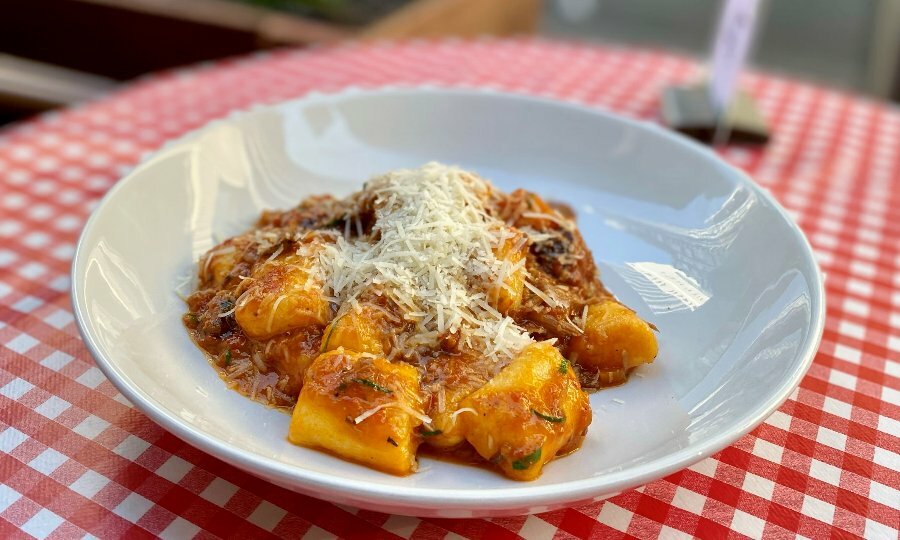 Bowl of gnocchi in a Napoli sauce with parmesan on a table with a red and white checked table cloth.