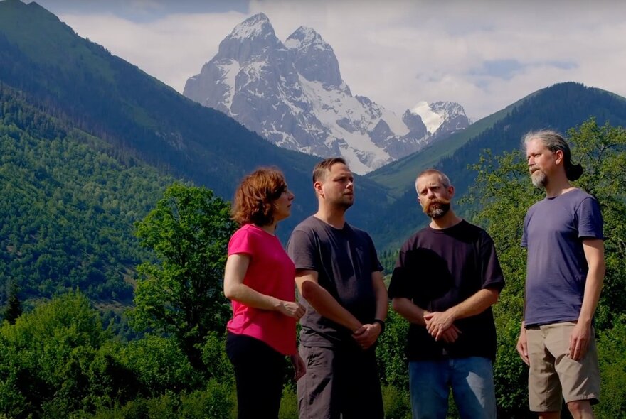 Four people standing together with an alpine scene in the background. 
