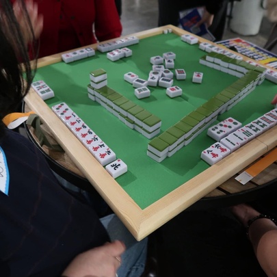 A green mahjong table with lines of tiles, people sitting around the table playing the game.