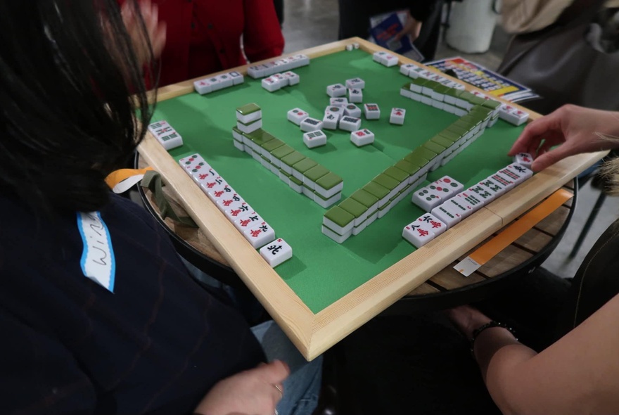A green mahjong table with lines of tiles, people sitting around the table playing the game.