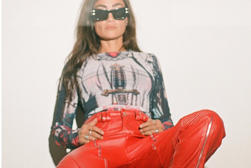 A person wearing a graphic print top, red pants, and sunglasses.