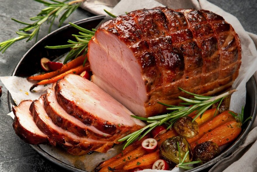 A glazed Christmas ham on a tray with roast carrots and rosemary garnish.