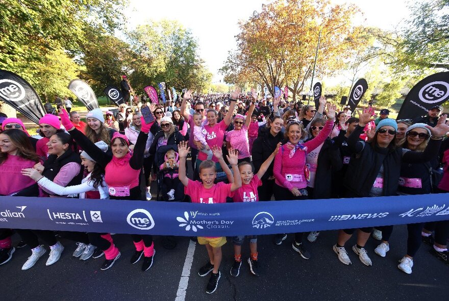 A mob of runners participating in the Mother's Day Classic fun run as they wait at the race start line behind a wide starting ribbon.