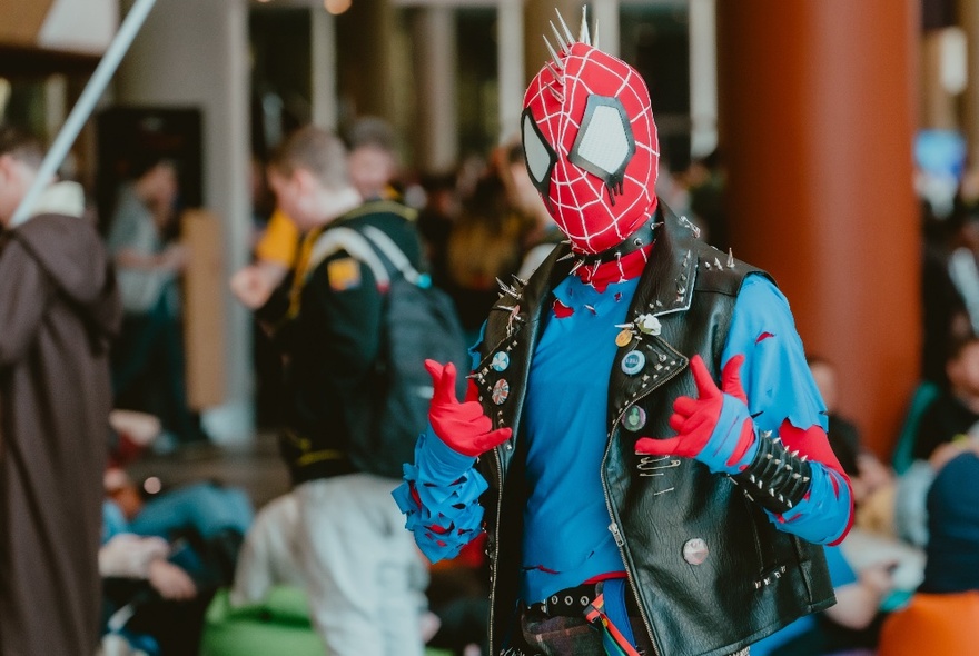 A person dressed as Spiderman with a sleeveless leather jacket over the top. 