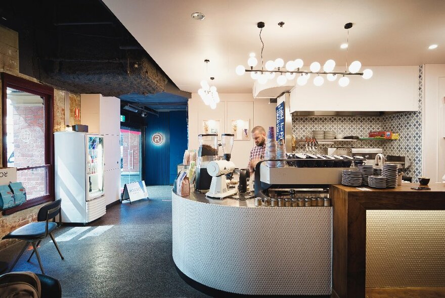 Modular cafe interior with barista at a coffee machine on a rounded white counter.