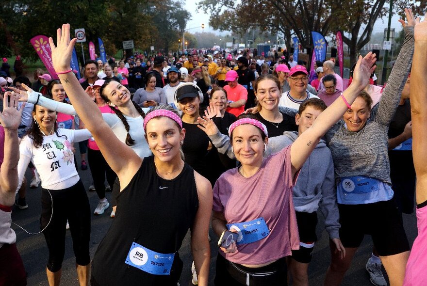 A large group of Mother's Day Classic fun run participants, holding up their arms and smiling, at the start or finish line of the Mother's Day fun run classic.