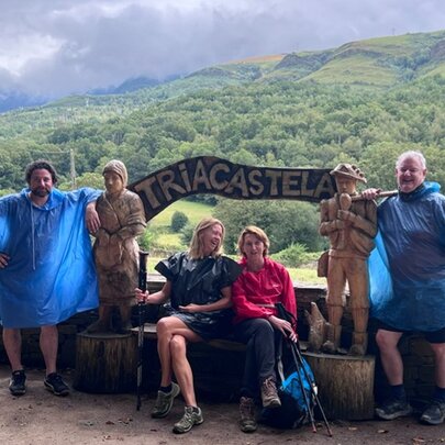 A group of walkers resting in Triacastela, Spain, during their journey on the Camino de Santiago, with green hills in the background.