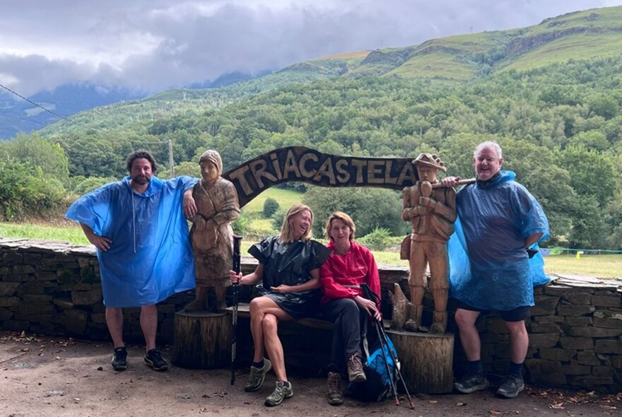 A group of walkers resting in Triacastela, Spain, during their journey on the Camino de Santiago, with green hills in the background.