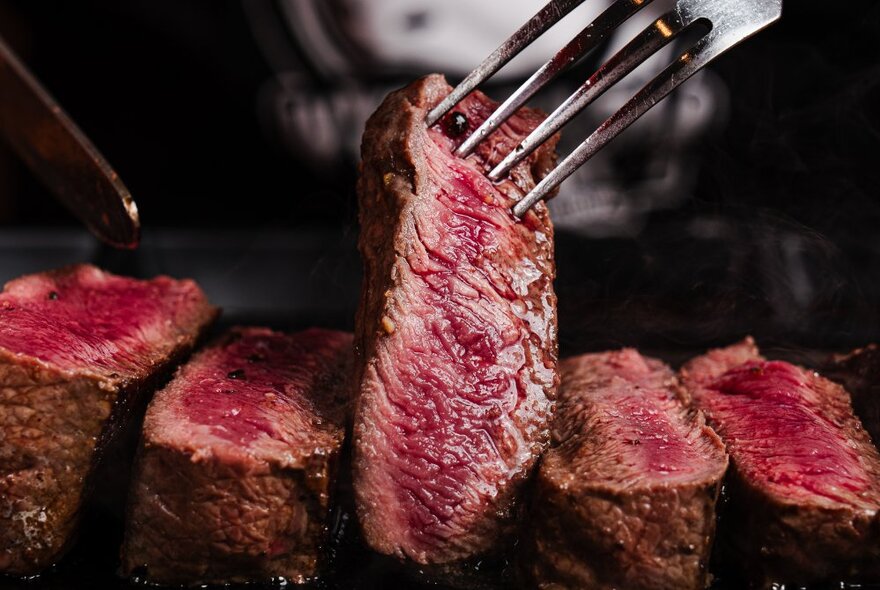 A fork lifting a slice of medium-rare steak from a plate.