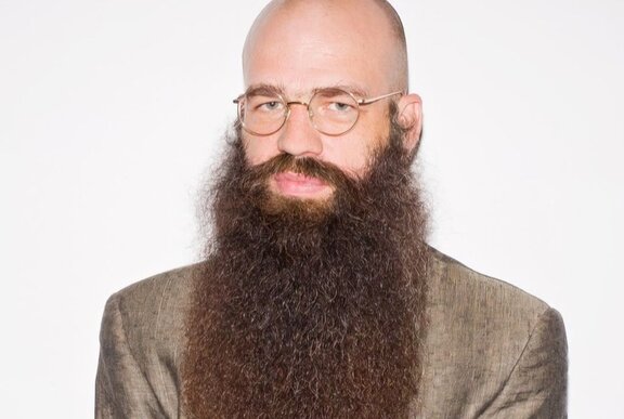 Artist Julius von Bismarck, with a bald head, thin-rimmed round glasses, and a long, full brown beard. 