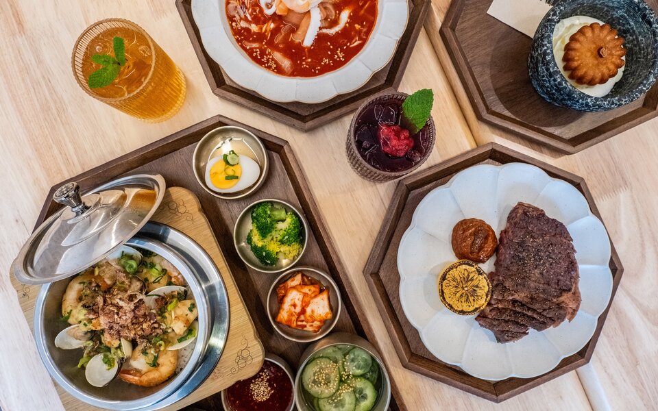 Korean dishes served on plates and in a steel pot with an assortment of small sides and drinks.