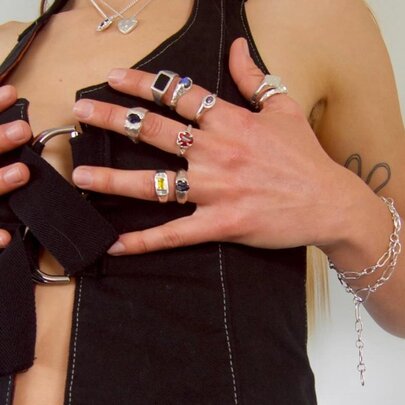Model wearing a black waistcoat, holding her hands covered in rings over her chest.
