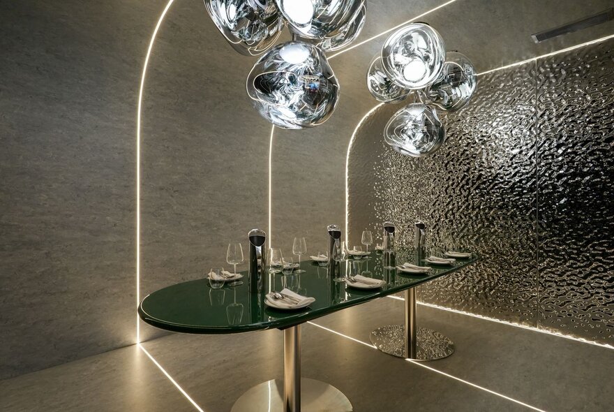 Private dining room with modern silver sculptural lighting, black oval table and tiled feature wall.