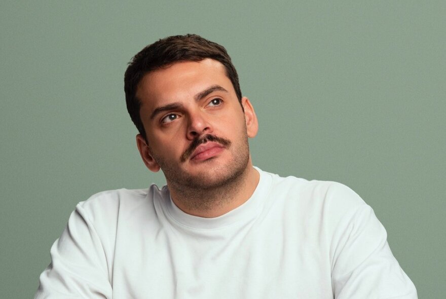 Man with moustache looking pensive, image cut off above the elbows.