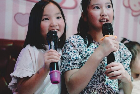 Two primary school aged children singing into karaoke microphones.