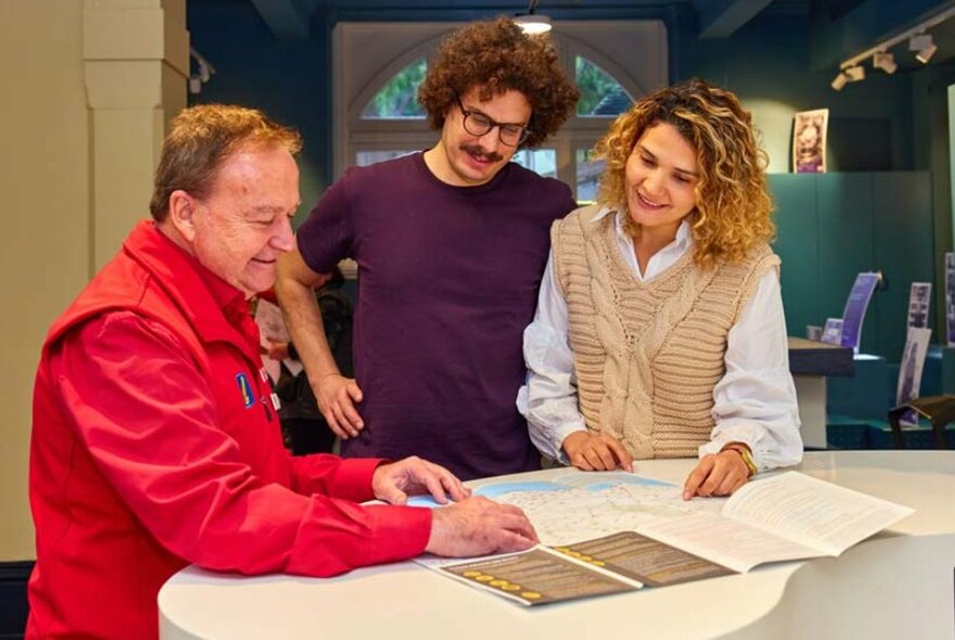 A man in a red jacket showing a woman and a man a map