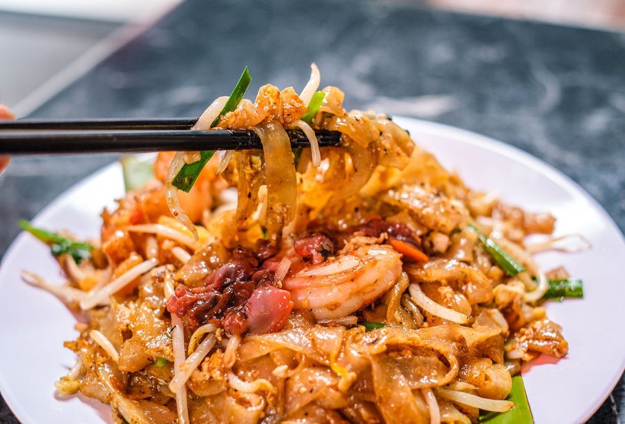A pair of chopsticks lifting noodles off a restaurant dish. 