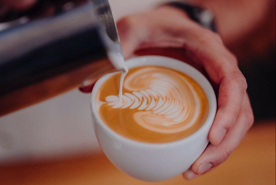 Frothed milk being poured into a cup of coffee to create a decorative pattern.