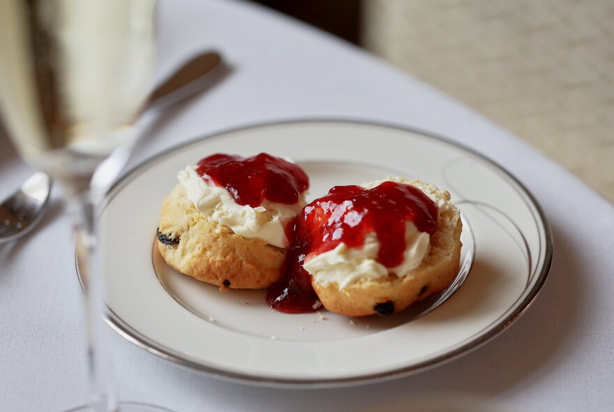A plate with two scones with cream and jam on top/