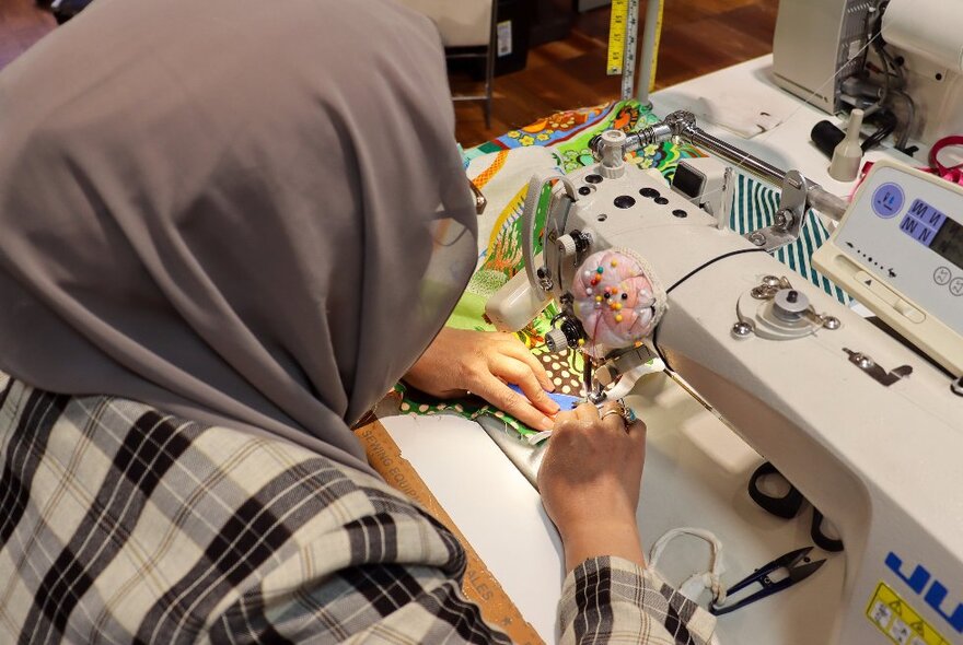 Woman wearing a headscarf working at a sewing machine with fabric.