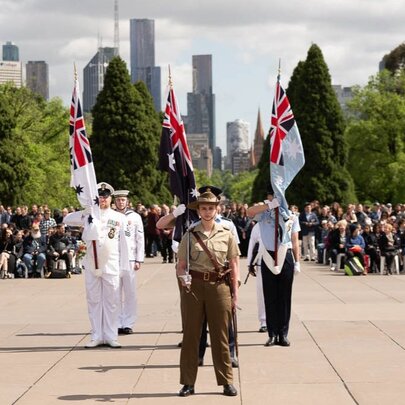 Service people standing on the forecourt of the Shrine with city buildings and massed crowds in the background.