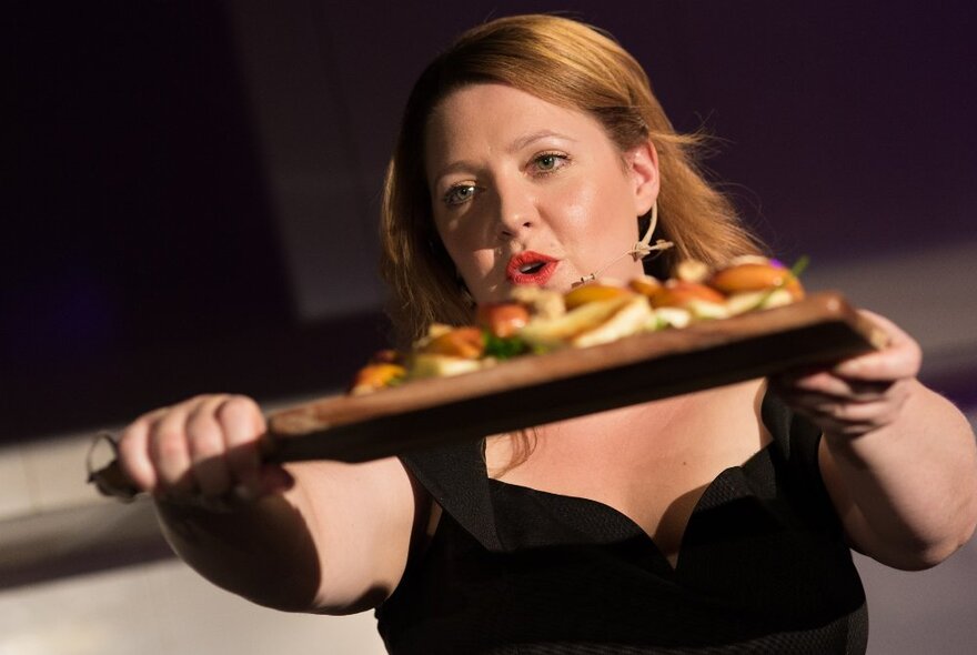 A woman holding forth a wooden board with food on it. 