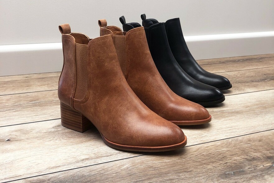 Two pairs of ladies leather elastic-sided boots, lined up on a wooden floor.