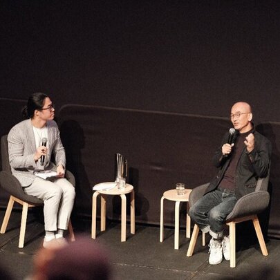 Two people sitting on a black stage, having a conversation.