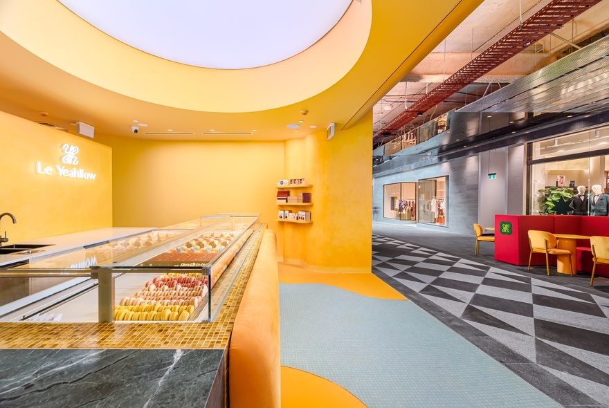 Cake shop interior with orange walls, circular ceiling and display cases, looking onto tiled arcade.