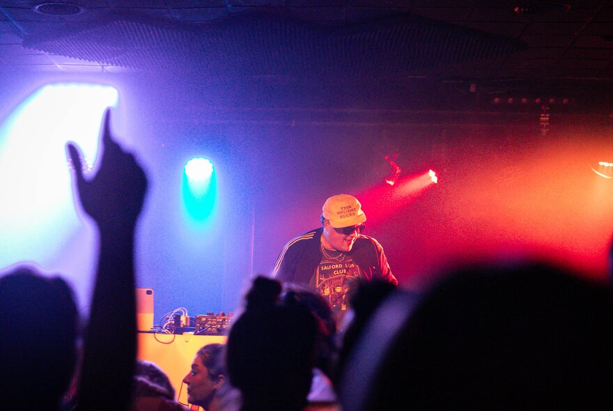 People dancing on a dance floor in a darkened club, to a DJ that is playing on the stage.