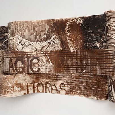 Exhibition piece of artwork on a blank wall, sepia illustrations with occasional words on an undulating surface.