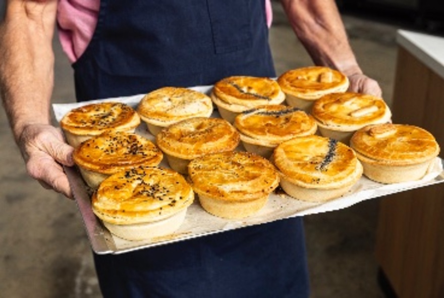 A tray of gourmet pies held by a baker in a dark blue apron.