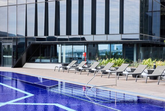 The blue lap pool at Vibe Docklands, with a row of day beds lined up along the edge of it.