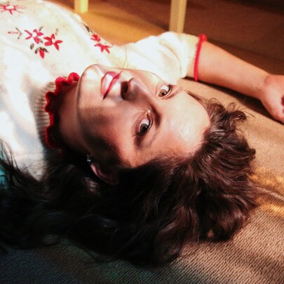 Musician, Maxon, lying on the floor wearing a delicate knitted jumper with embroidered red flowers.
