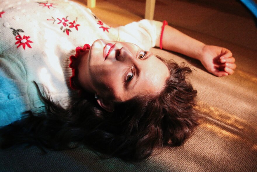Musician, Maxon, lying on the floor wearing a delicate knitted jumper with embroidered red flowers.