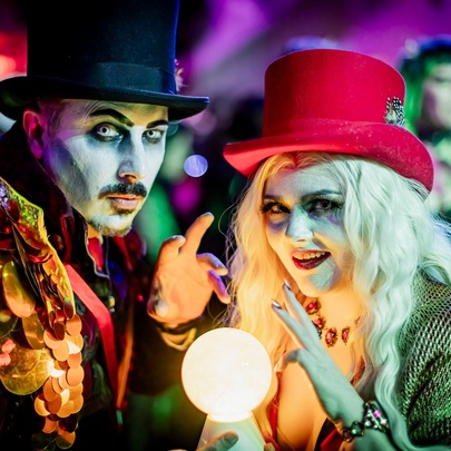 Two people in elaborate fantasy costumes and heavy makeup with an illuminated crystal ball between them. 