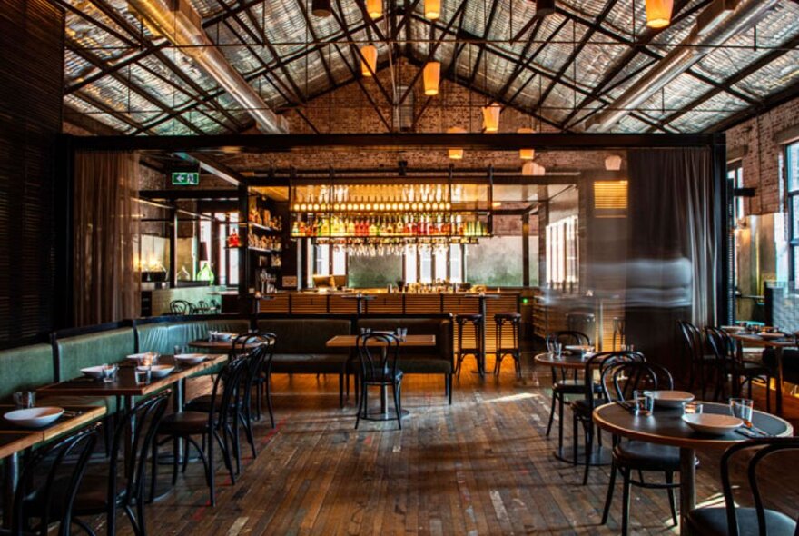 The interior of Thai restuarant, Longrain, with exposed beams and rafters, booth seating and round tables, with the bar in the background.