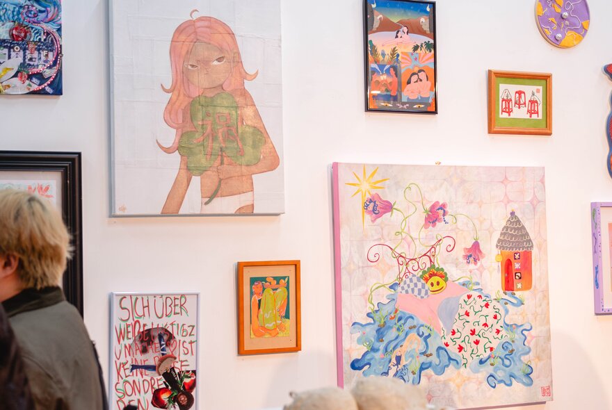 An exhibition of contemporary wall-based artworks in a gallery space, with a person in the foreground.