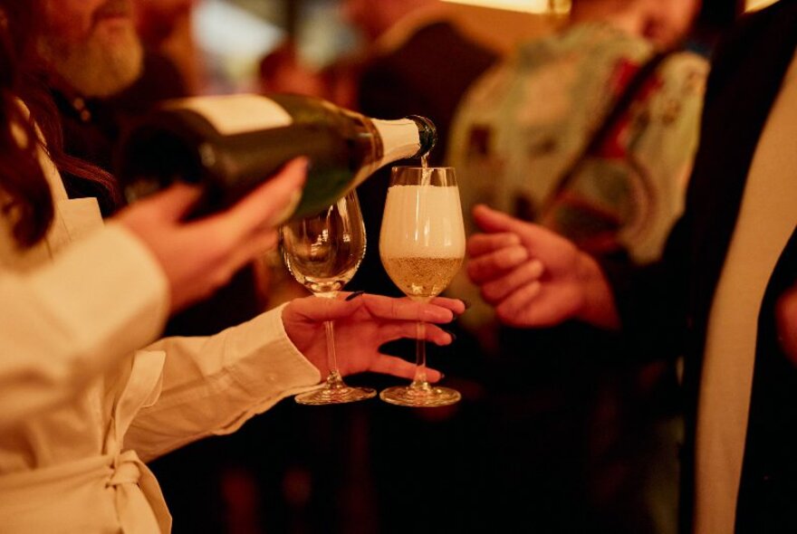 A waiter pouring glasses of champagne with a hand ready to accept a glass. 