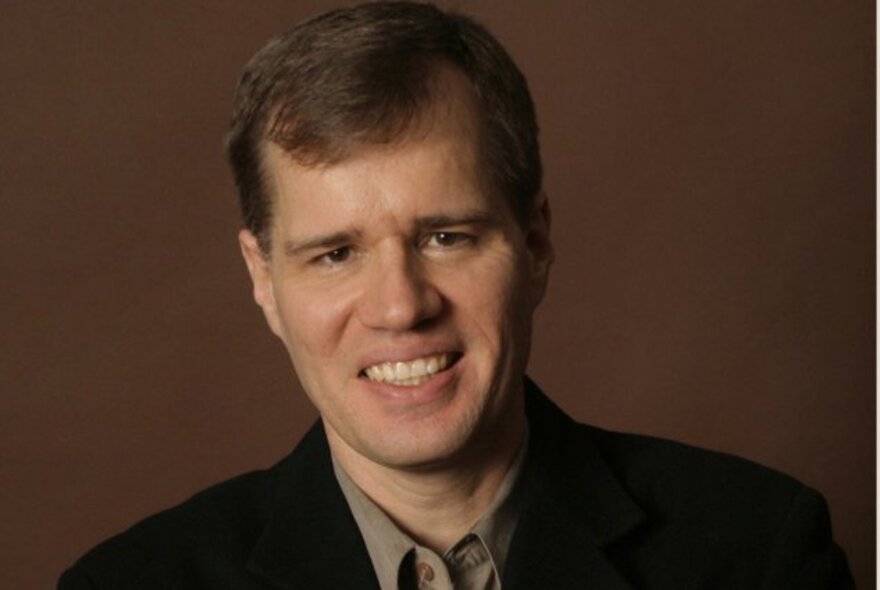 Musician John Novacek, smiling with grey shirt.