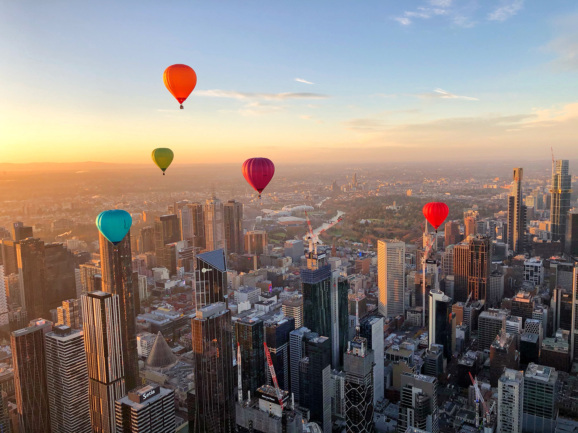 Colourful hot air balloons flying over the Melbourne city skyline at sunset.