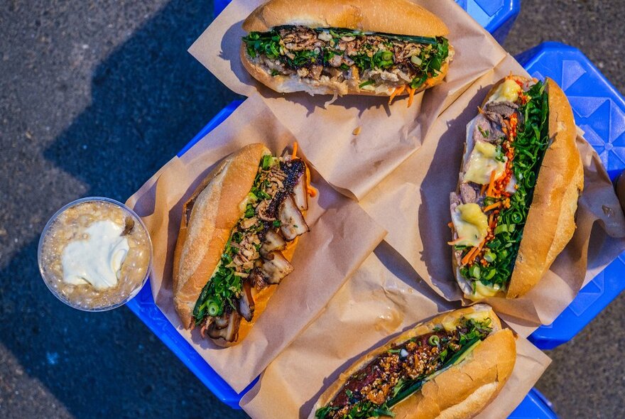 A collection of banh mi sandwiches and a Vietnamese coffee on blue stools.