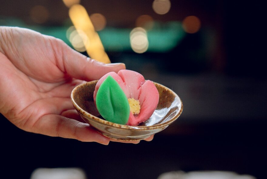 Hand holding a glazed bowl with a Japanese sweet shaped like a flower.