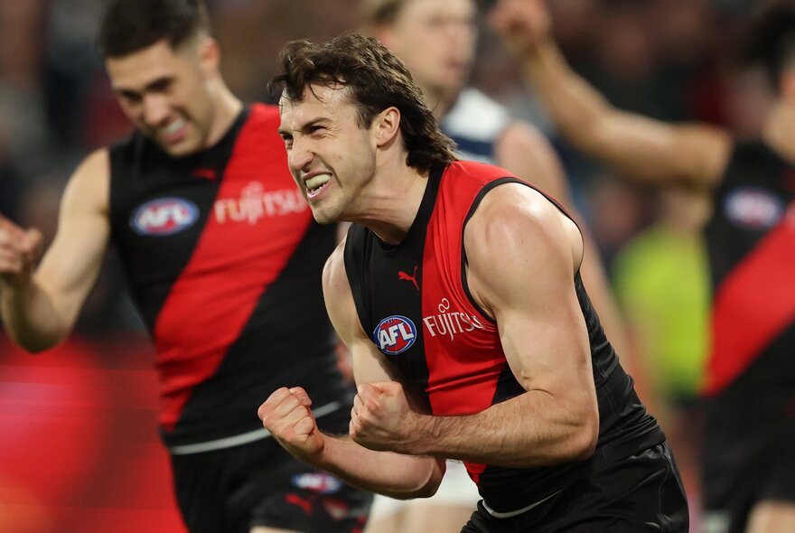 An Essendon football player celebrates emphatically with team mates.