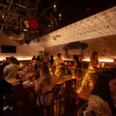 The inside of a dimly lit venue with patrons enjoying drinks at bar tables.