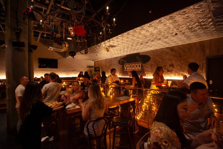 The inside of a dimly lit venue with patrons enjoying drinks at bar tables.