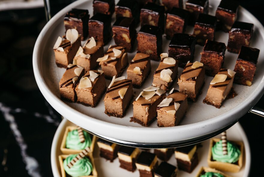 A two-tiered white serving tray filled with various bite-sized gourmet chocolate desserts.
