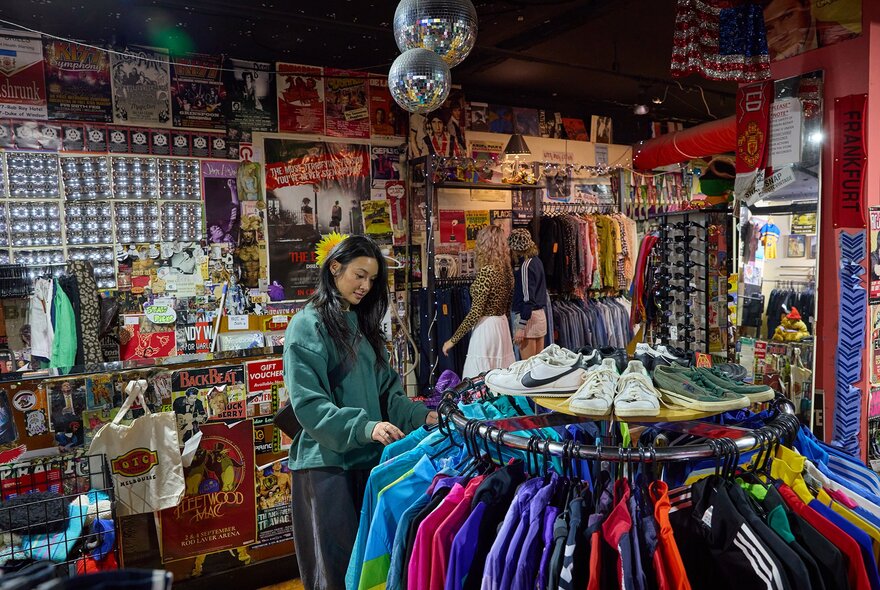 A woman browsing a rack of retro jackets in a colourful vintage shop with disco balls.